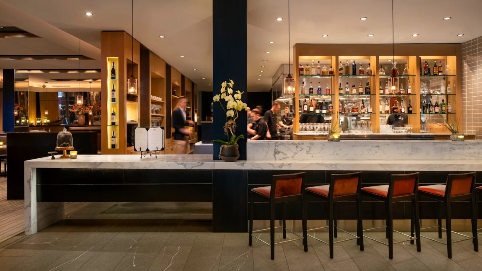 Sophisticated bar area at La Toque restaurant with marble countertop, leather bar stools, illuminated liquor display shelves, and modern pendant lighting in an upscale dining space.