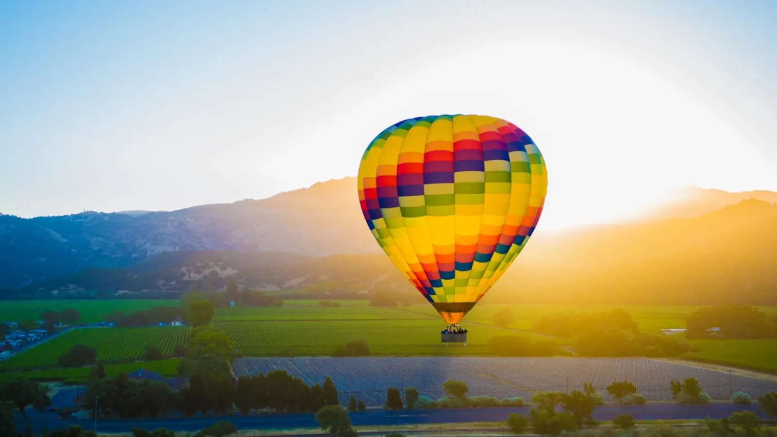 A colorful hot air balloon floats peacefully during a sunrise balloon flight napa valley experience, drifting above rolling vineyards and farmland at golden hour.