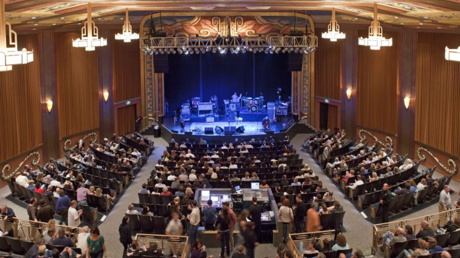 The Uptown Theatre Napa features an elegant historic auditorium with ornate wooden paneling, sophisticated lighting, and a packed audience enjoying a live performance on stage.