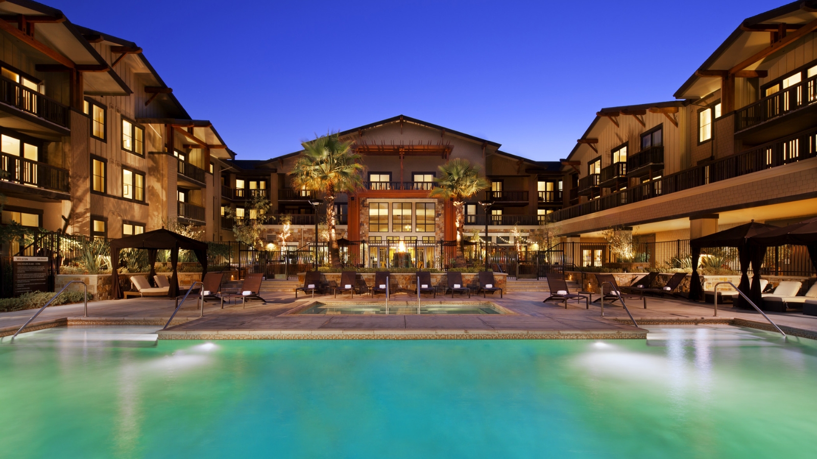 Archer Hotel Napa evening view featuring illuminated luxury resort architecture with glowing pool, lounge chairs, and Mediterranean-style courtyard at dusk