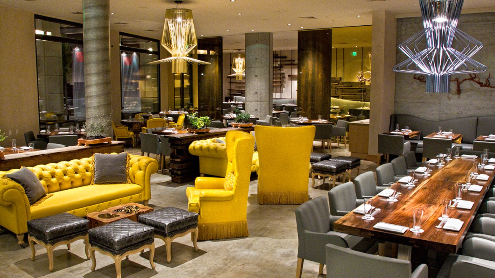 Morimoto Napa - contemporary fine dining restaurant with bold yellow velvet seating, wooden dining tables, gray upholstered chairs, geometric pendant lighting, concrete pillars, mirrored bar area, and modern minimalist design creating an upscale Japanese-inspired atmosphere
