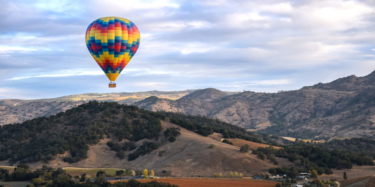A colorful hot air balloon drifts over rolling Napa Valley hills during a sunrise balloon flight, a signature experience offered by Napa Valley Balloons.