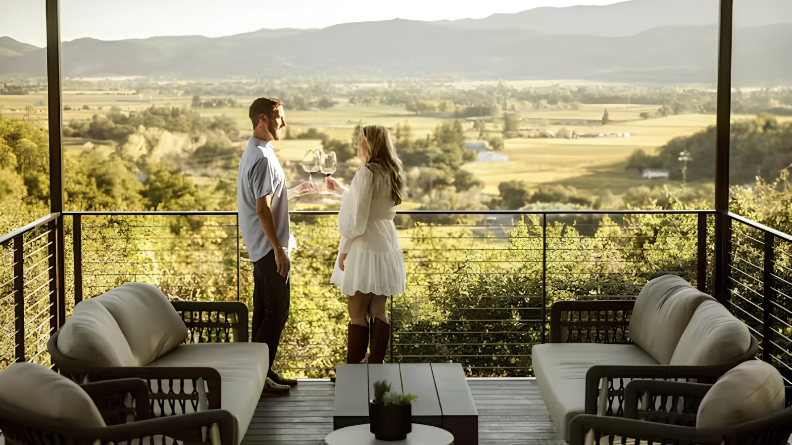 A couple toasts wine glasses on a scenic terrace overlooking the valley, capturing the elevated experience offered by St Helena tasting rooms.