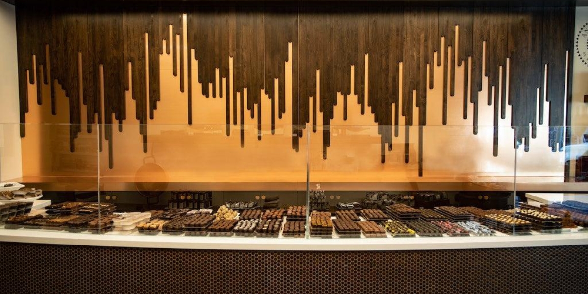 A glass display case filled with an assortment of handcrafted chocolates sits beneath a dramatic wooden wall feature at Anette’s Chocolates.