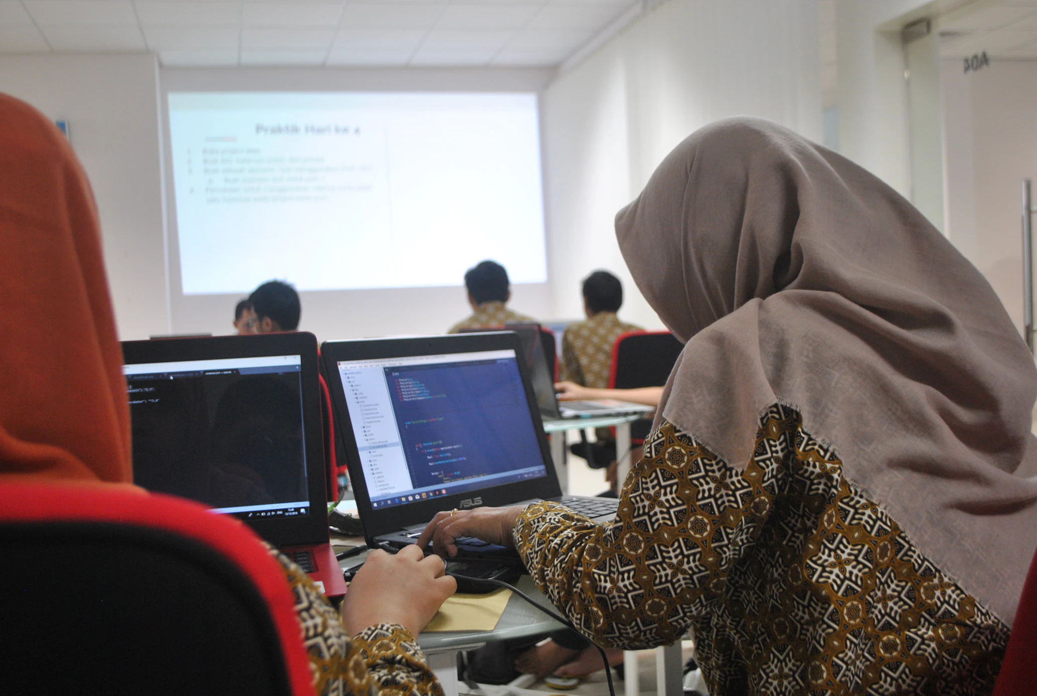 Financial and digital literacy. Two women wearing hijabs sitting at a table, looking at a tablet together in a bright office setting.