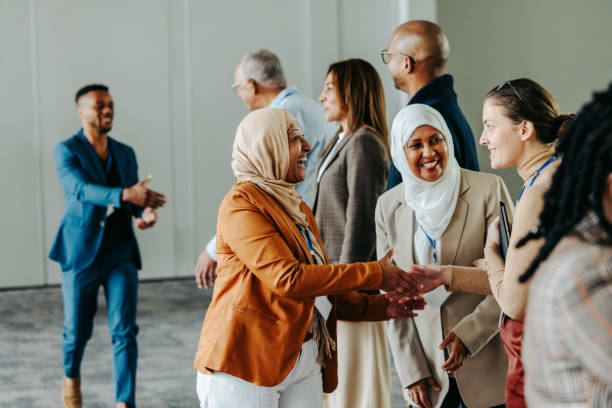Employment Connection. A young woman in a hijab shaking hands with another woman at a career opportunities event with other young people in school uniforms in the background.