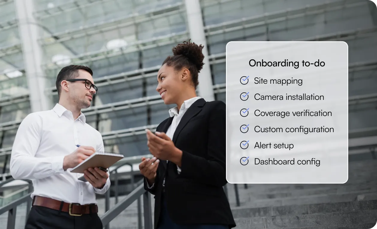 Two business professionals discussing in front of modern glass building with onboarding to-do list displayed, including site mapping and camera installation.