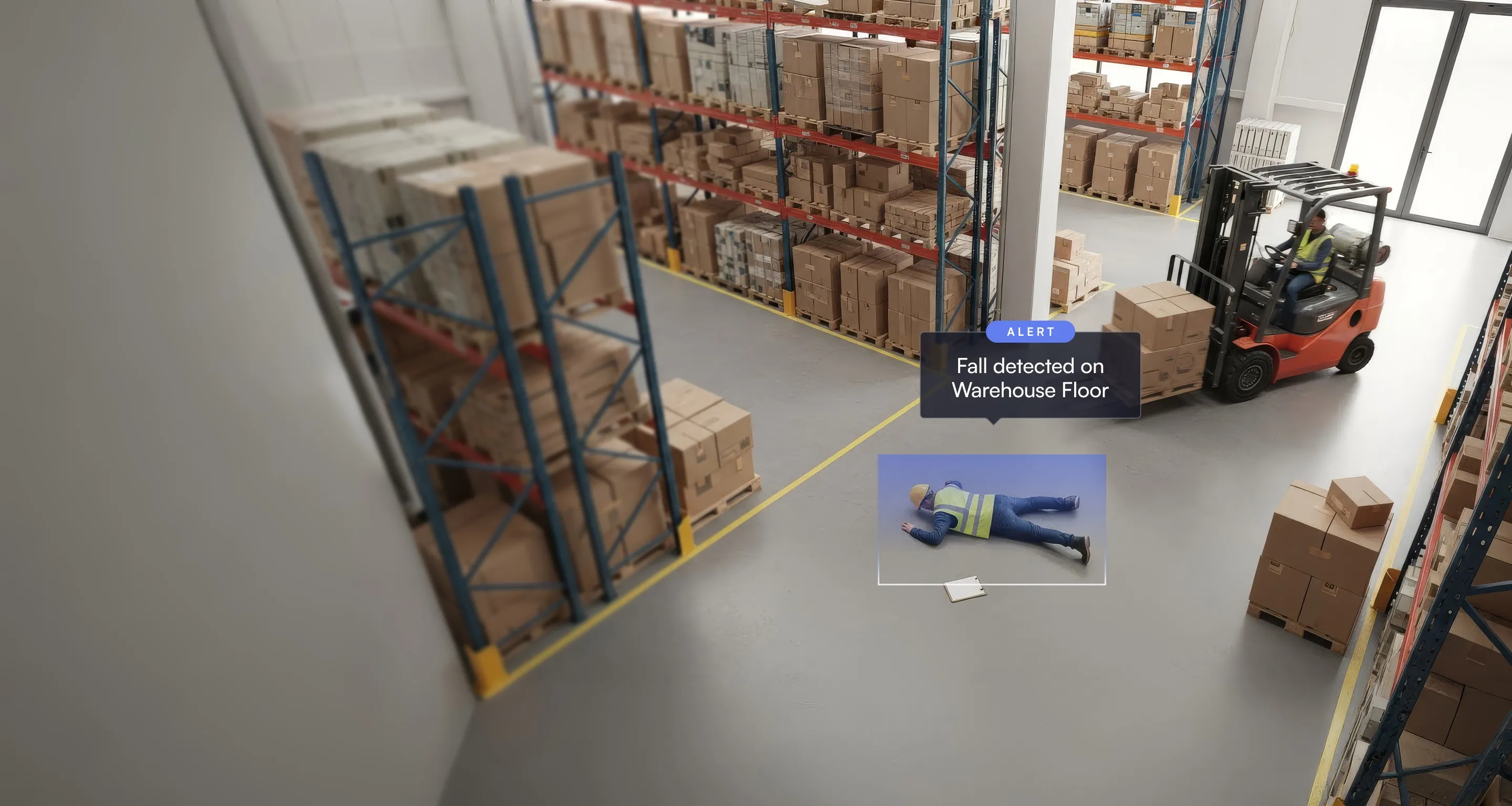 Warehouse with stacked boxes on shelves and a forklift nearby, a worker in a safety vest lying on the floor with an alert indicating a fall detected.