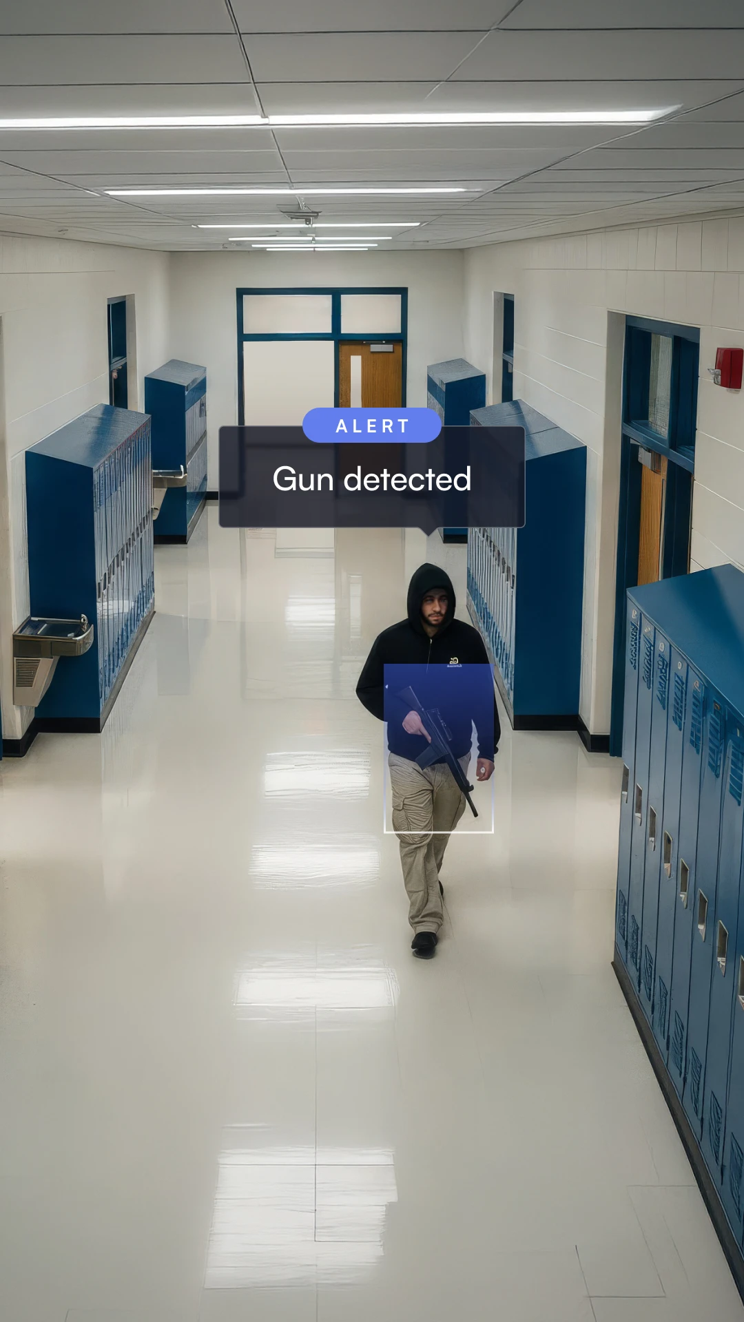 Male wearing a black hoodie walking down a school hallway carrying a gun, with an alert box saying 'Gun detected.'