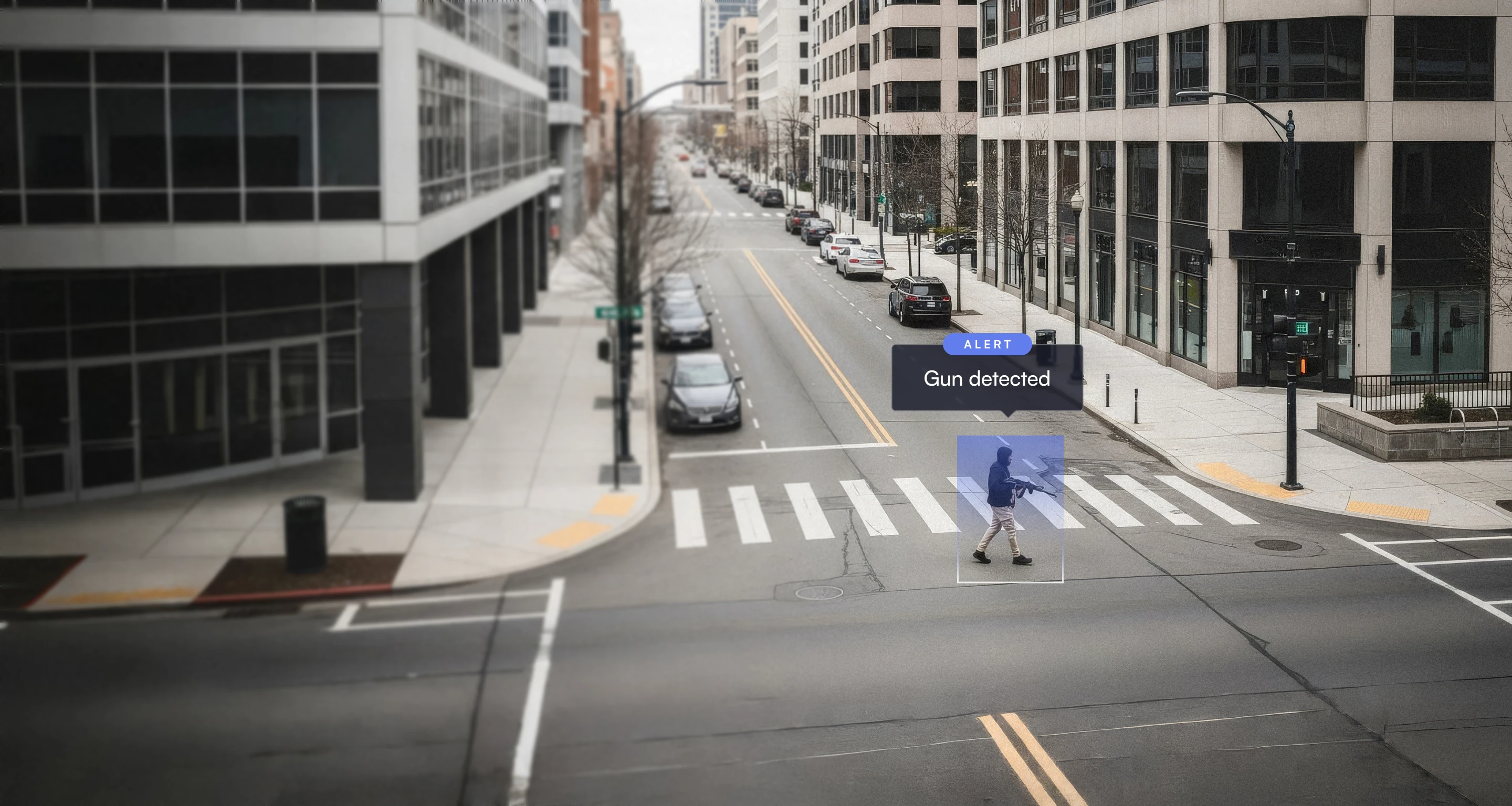 Urban street crosswalk with a person carrying a gun, highlighted by a detection box with a 'Gun detected' alert.