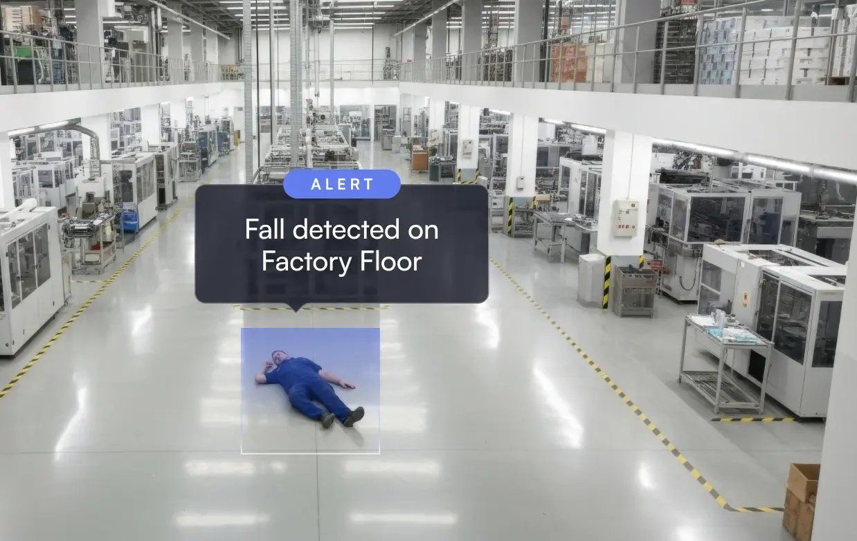 Man lying on factory floor with alert text saying 'Fall detected on Factory Floor' in a large industrial workspace.