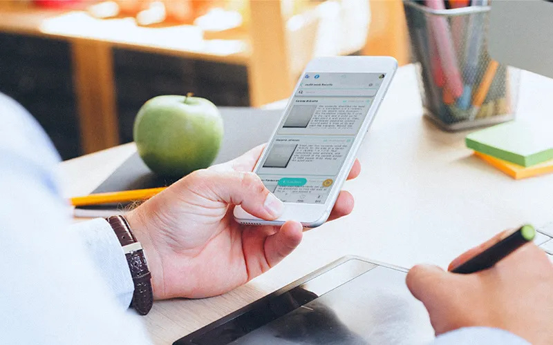 Educator scanning paper assignment with smartphone using K-12 GRADED+ app for instant auto-grading and feedback