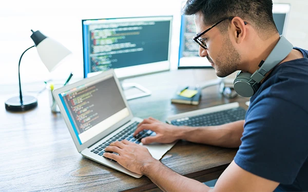 Web specialist coding school site update on dual-monitor setup, illustrating 24-hour website update guarantee