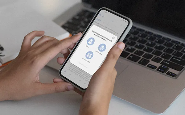Hand holding smartphone displaying secure login screen for K-12 school app beside a laptop computer