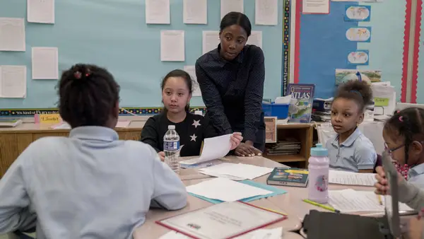 Teacher guiding small-group reading with elementary students in a classroom — candid photo.