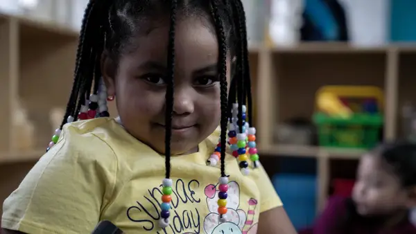 K-12 student with beaded braids smiling in classroom — candid portrait.