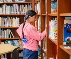 Student choosing a book from the shelves in the school library