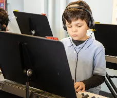 Elementary student wearing headphones while practicing keyboard during a music class