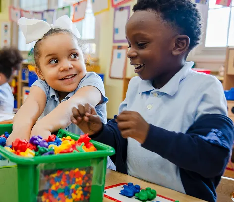 Two elementary students smiling and playing with colorful counting bears during a classroom learning activity.