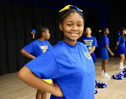 Student cheerleader smiling during after-school cheer practice on stage.