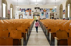 Student walking through the center aisle of the school auditorium with rows of wooden seats