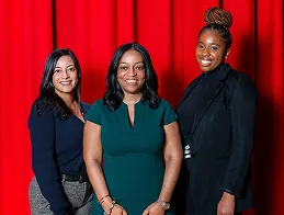Three staff members posing together in front of red stage curtains