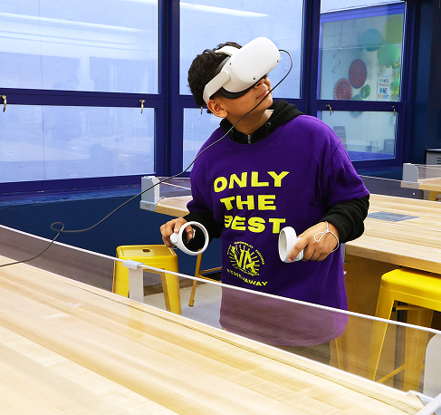 A student wearing gloves and a purple hoodie tending to a green climbing plant, looking through the leaves.