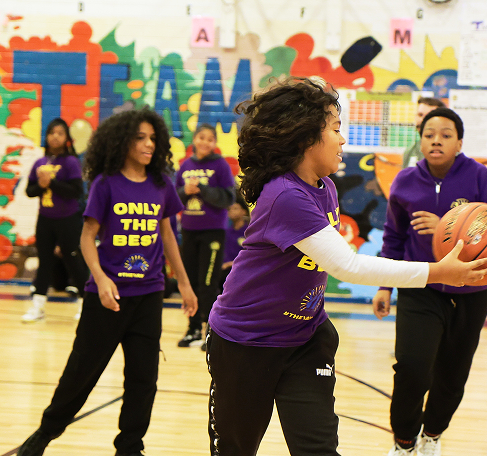 A group of students in a gymnasium playing basketball during a school sports activity.