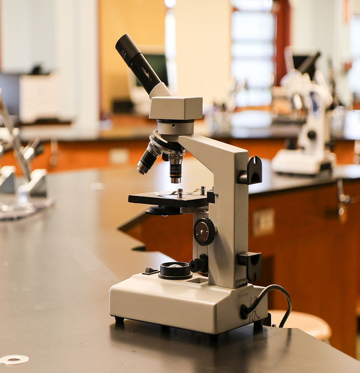 A close-up of a compound microscope sitting on a black laboratory table in a science classroom