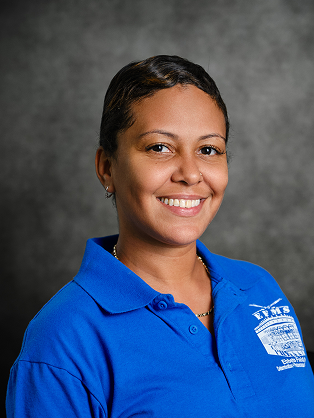 A staff member with dark hair pulled back in a bun, smiling in a blue polo shirt.