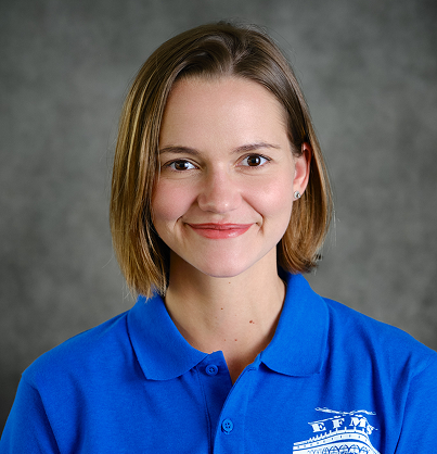 A smiling woman with chin-length brown hair wearing a blue Ebbets Field Middle School polo shirt against a grey background.