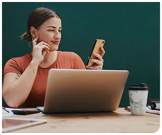 Teacher using STUDENT+ on her phone with a laptop in front of her