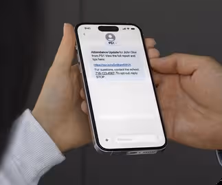 Close-up of hands holding a smartphone displaying a personalized attendance report SMS from a K-12 school