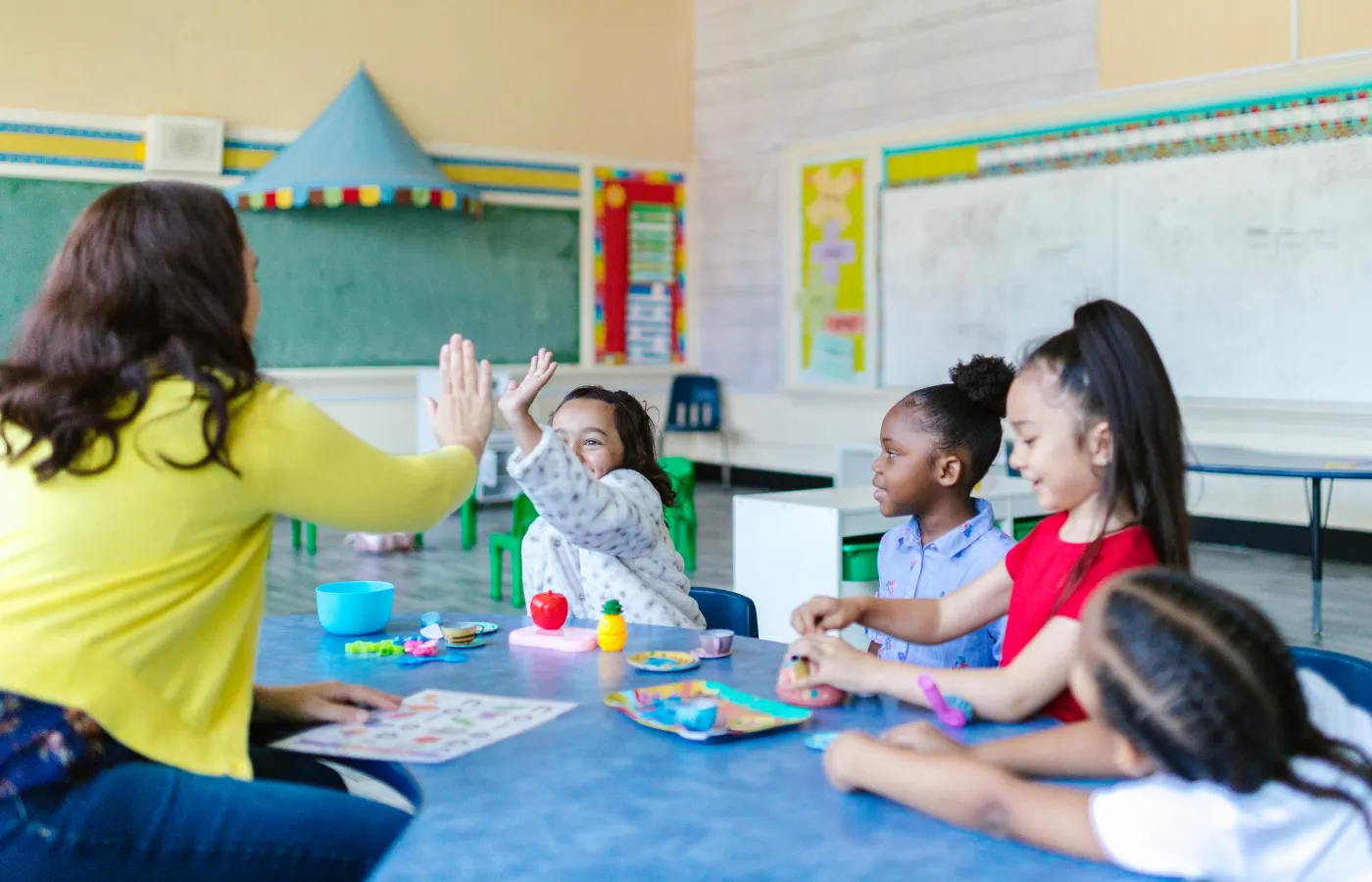 A vibrant classroom with students actively participating, including one about to high-five the teacher, showcasing the engagement, interaction, and sense of accomplishment fostered by the 3-2-1 Exit Ticket method.
