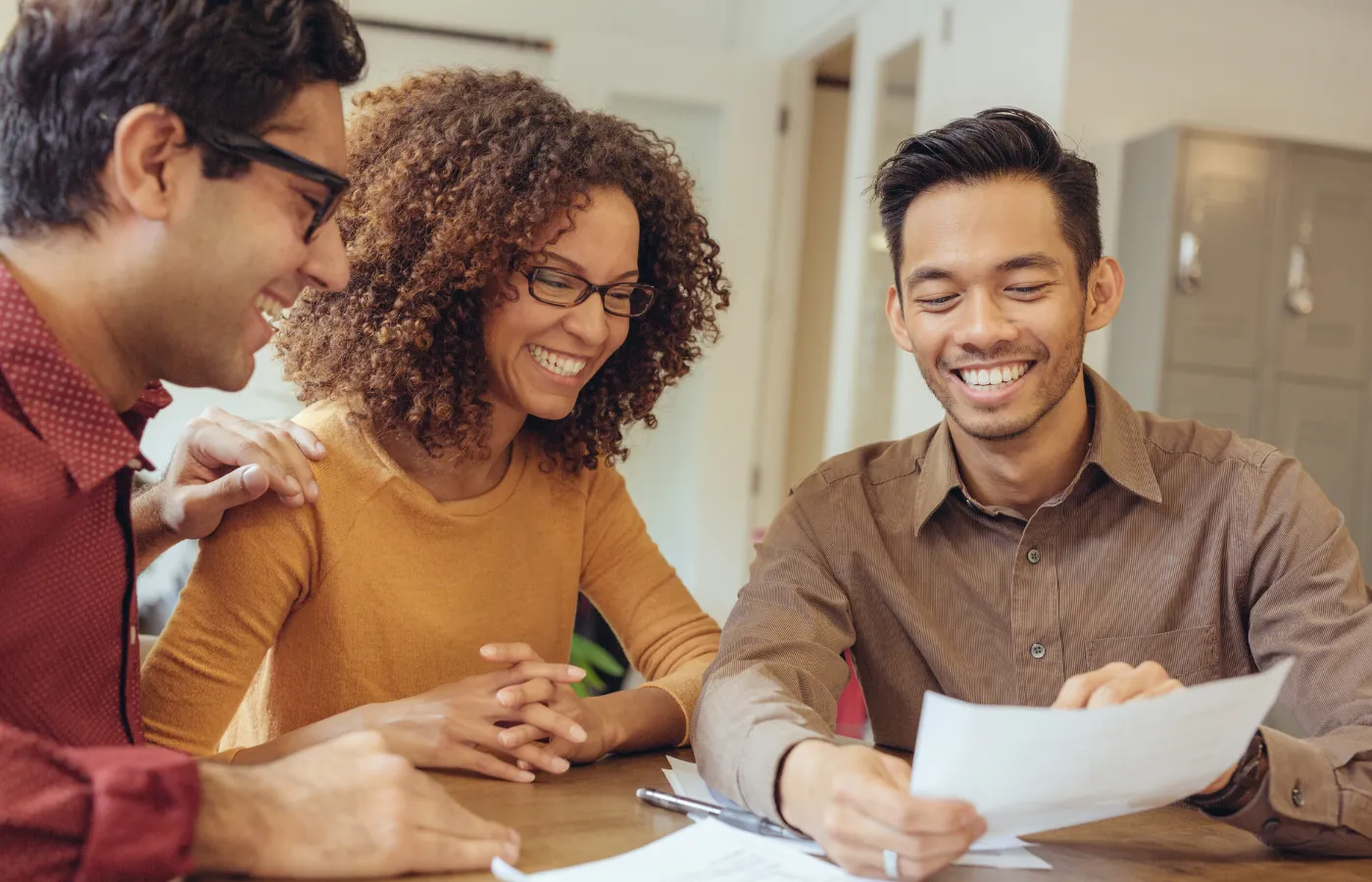 Three teachers smiling and discussing a piece of paper, symbolizing collaboration and the professional development opportunities offered by SOLVED Consulting for educators.