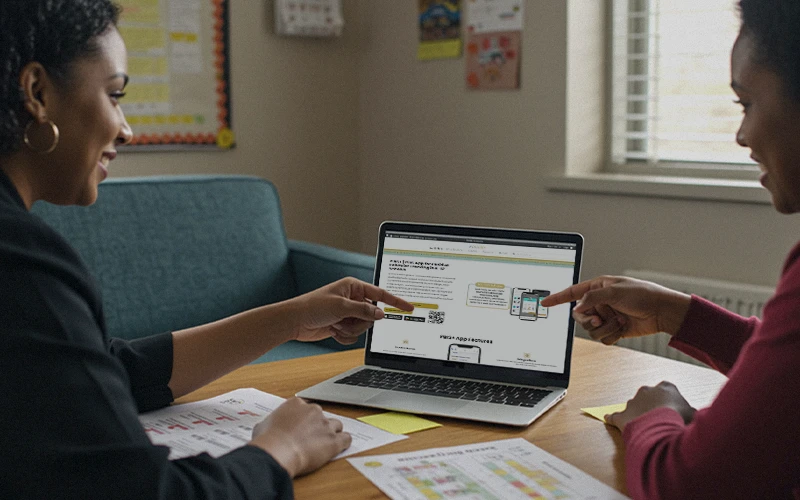 Two teachers review PBIS+ software on a laptop, pointing to digital behavior-tracking features next to printed reports