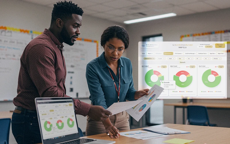 Two educators examine printed pie-chart report beside laptop displaying SOLVED dashboard overlays, aligning student-growth data.
