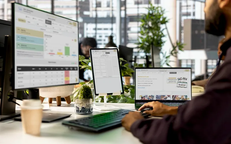 School leader reviewing SOLVED Data Dashboard with charts and student performance metrics on desktop and laptop screens in an office setting
