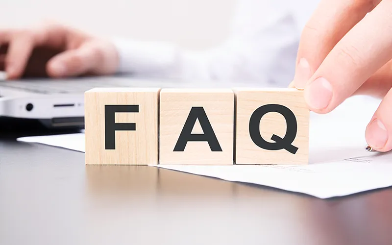 Hand arranging wooden blocks that spell FAQ, representing frequently asked questions for PLC processes.