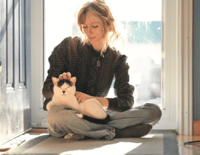 A young women with her cat is sitting in the window.