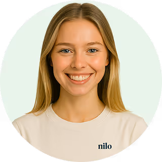 Smiling young woman with long blonde hair wearing a white shirt against a light background.