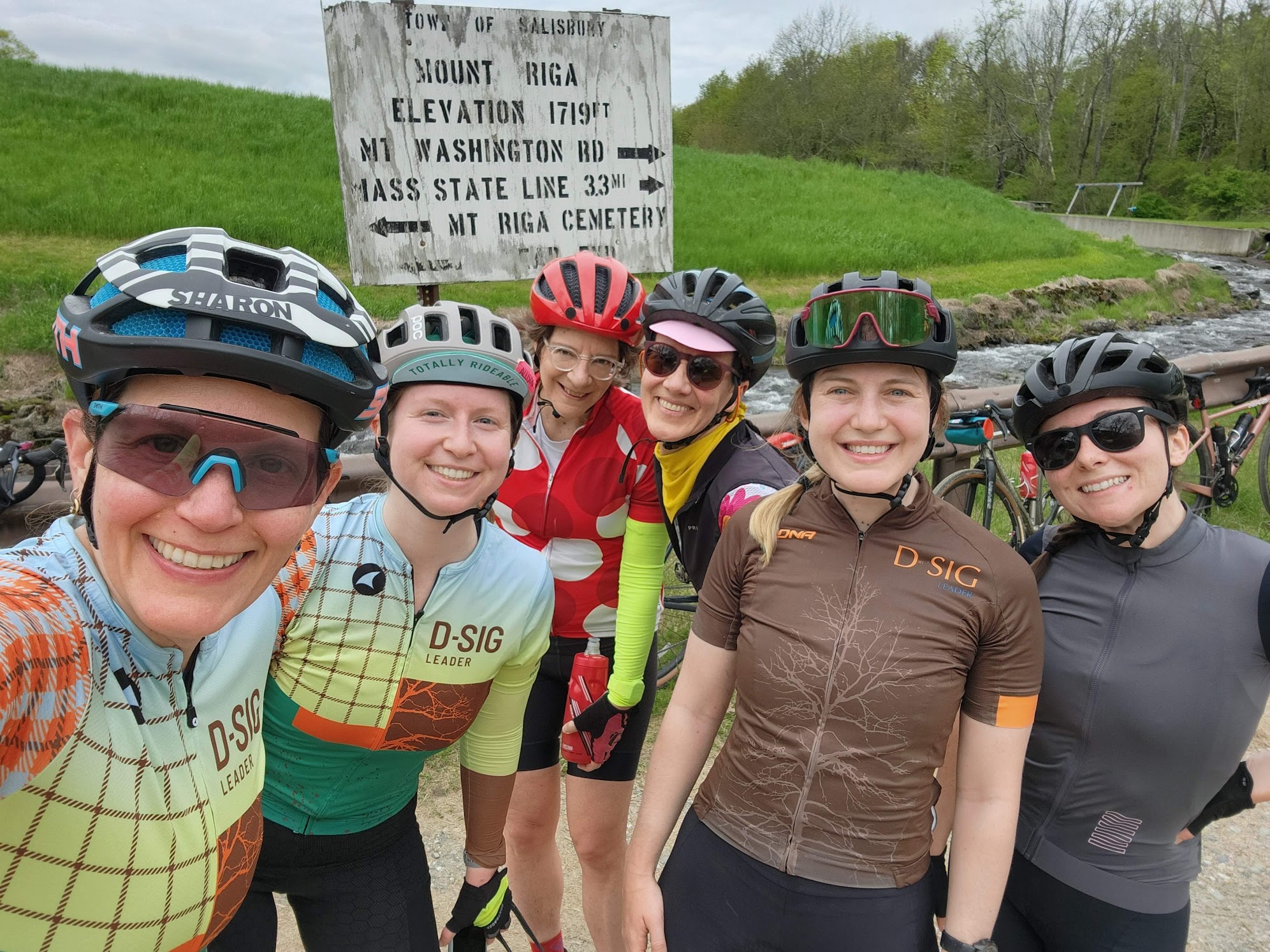D-SIG riders smiling in front of a Mount Riga road sign