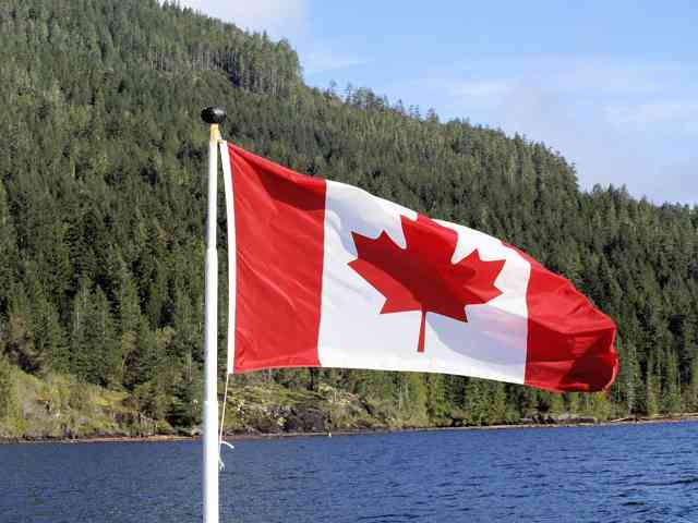 Canadian flag waving by lake with forested mountains in background