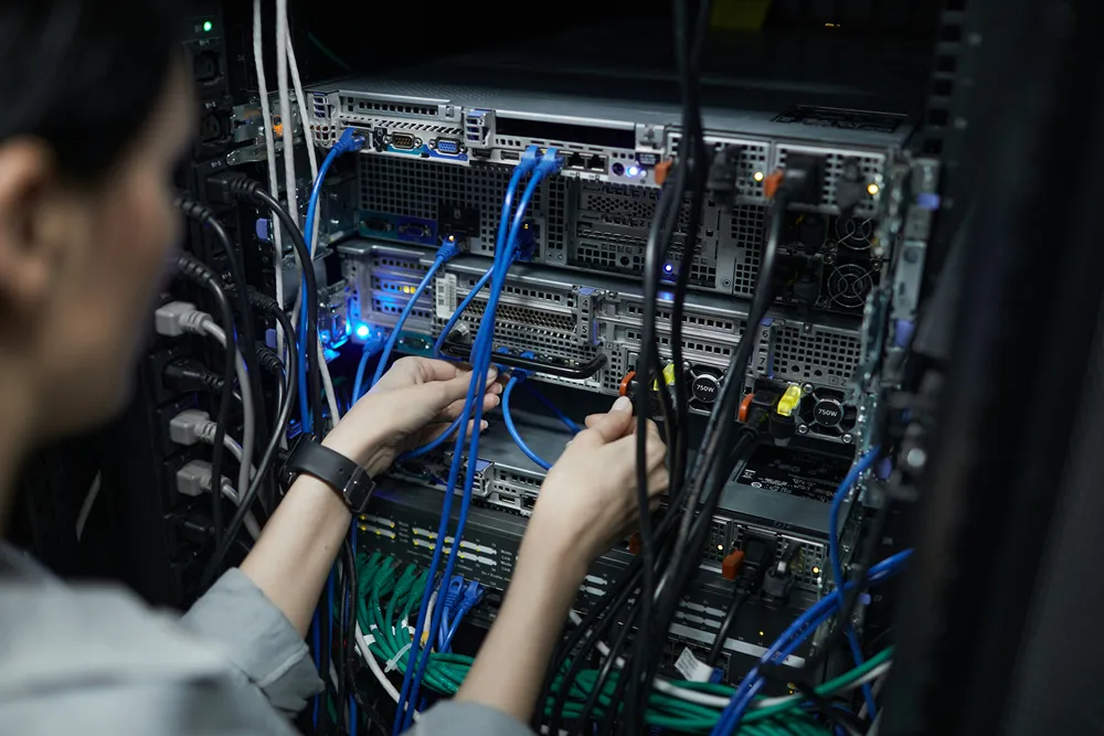 Network technician connecting cables in a data center server cabinet