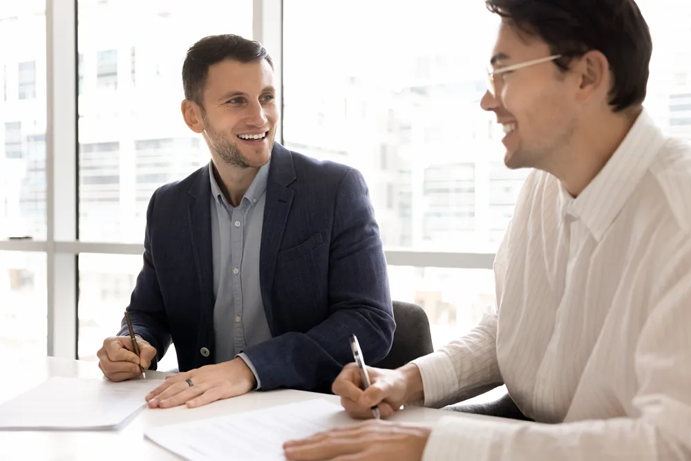 Two businessmen at a conference table signing a procurement contract.