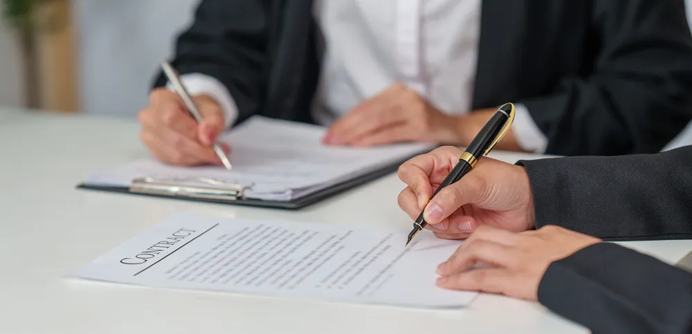 Close-up of business partners signing a legal contract document.