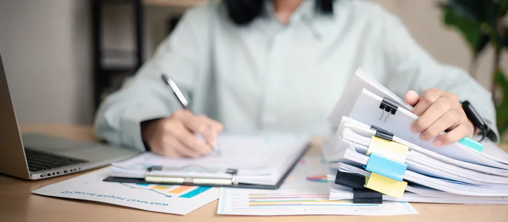 Business professional auditing a stack of documents at an office desk.