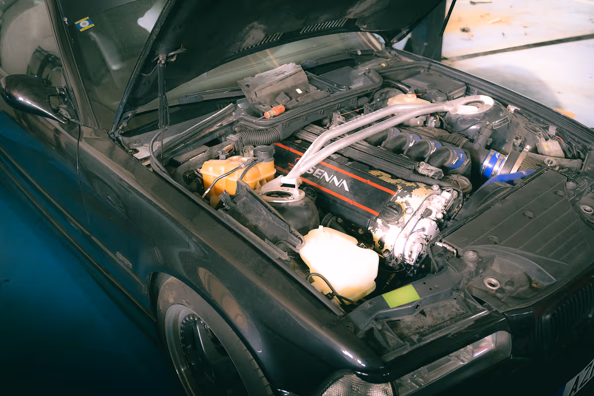 Open hood of a black car showcasing a detailed engine bay with a red and black engine cover labeled 'SENNA' and various visible components.