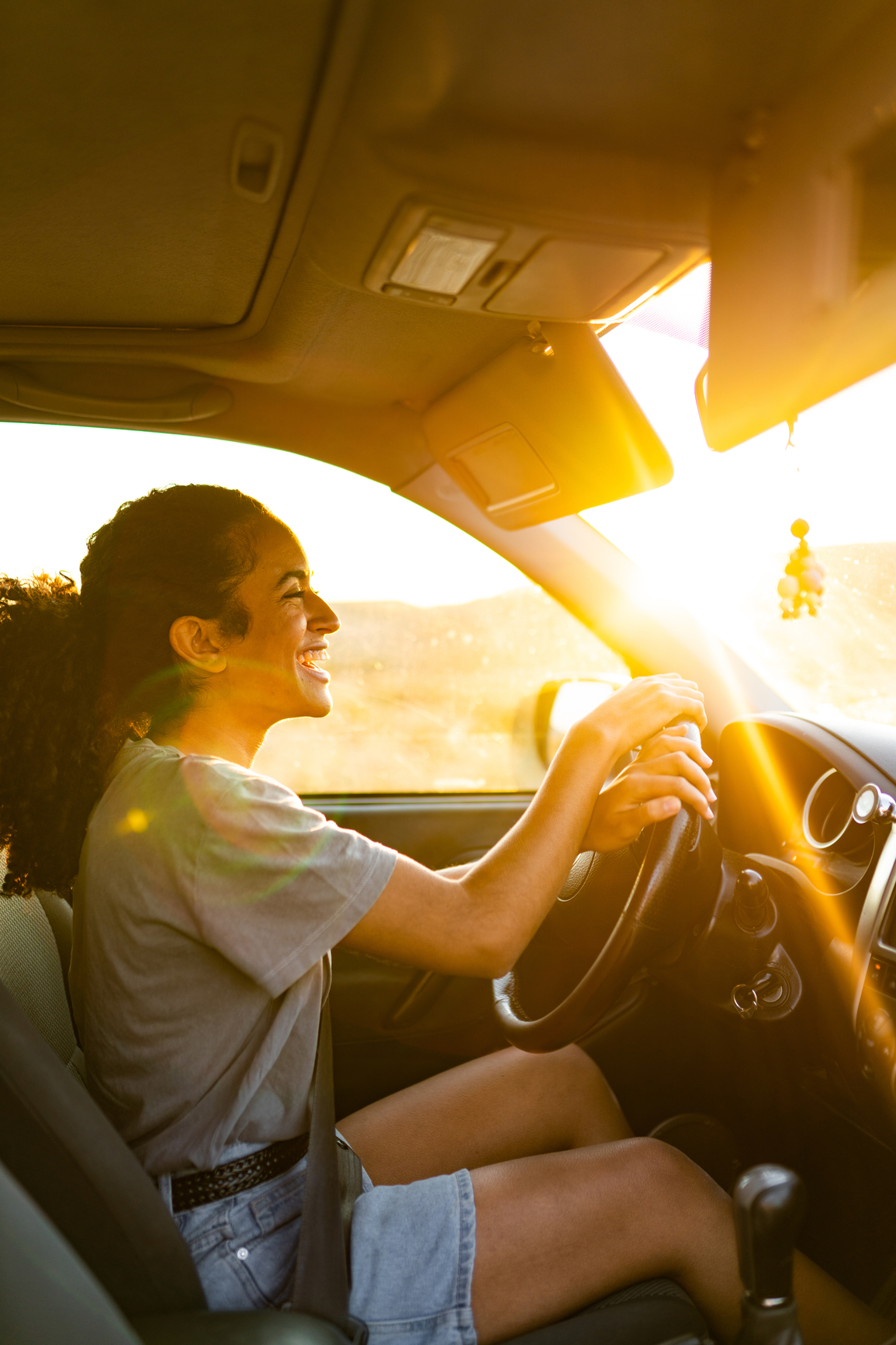 A person sat in the driving seat of a new car, the sun is shining though the window and they are happy