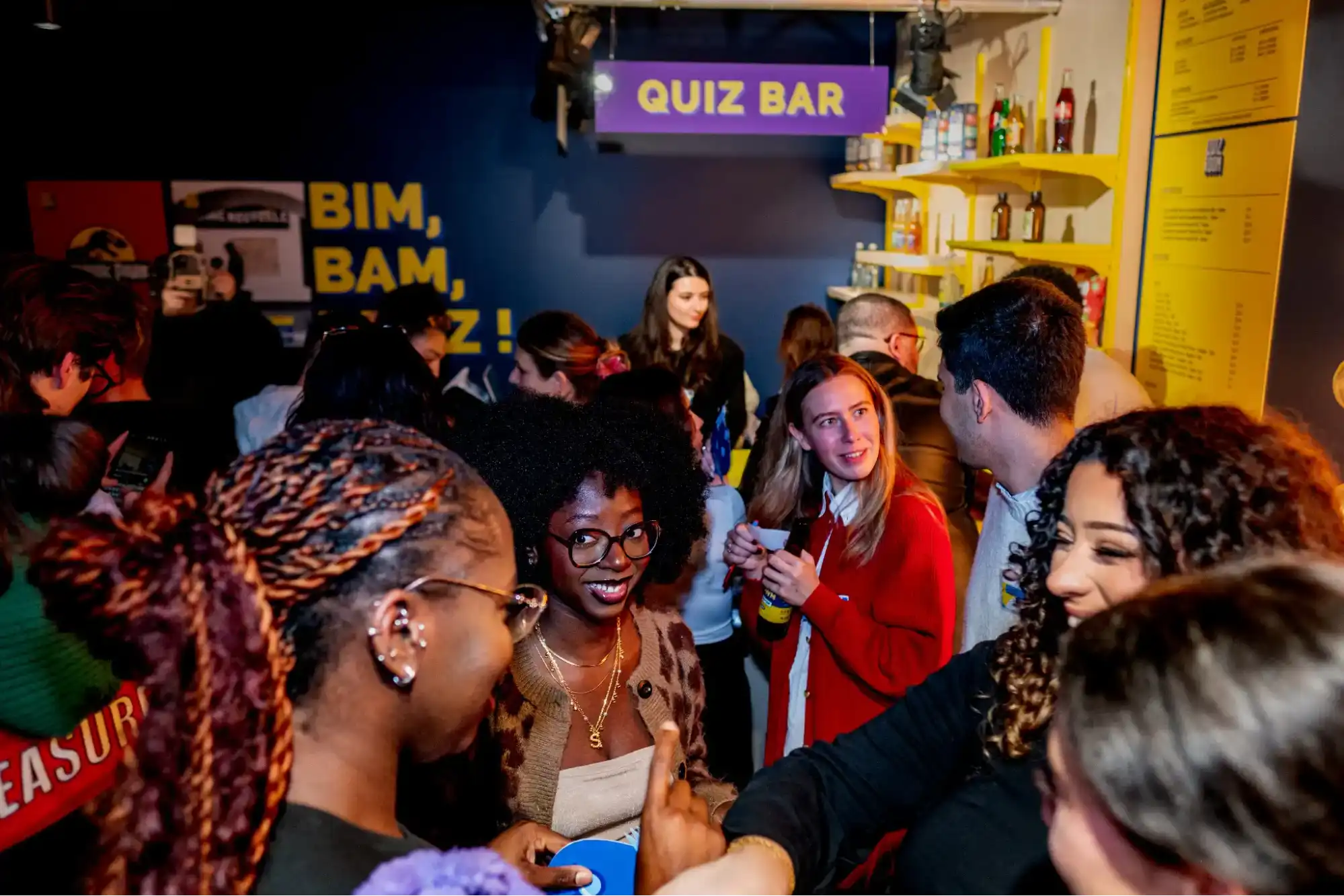 Regroupement de personnes avec des boissons au bar d'une salle Quiz Room, panneau "Quiz Bar" dans le fond